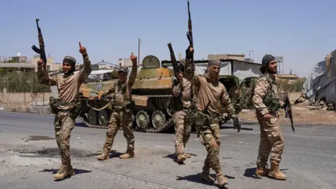 Reuters Syrian security forces celebrate by raising their rifles during clashes with Druze fighters in Suweida city, southern Syria (16 July 2025)