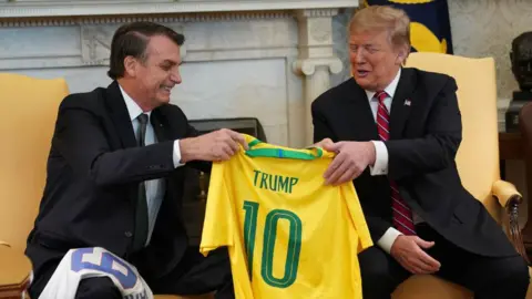 Getty Images Jair Bolsonaro presents Donald Trump with a Brazilian football shirt which reads "Trump 10" on the back
