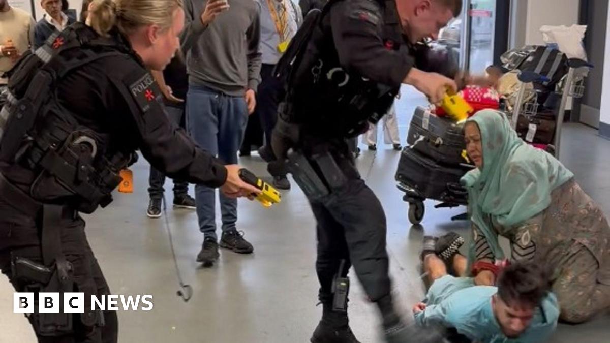 A mid shot of Muhammad Amaad walking towards the camera. He has short dark hair, a long dark beard and is wearing glasses and a black suit and tie.