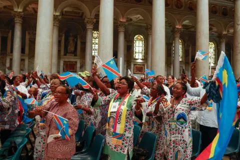 AP A congregation of mainly women from DR Congo cheering in the Papal Basilica of St Paul Outside the Walls in Rome, some waving Congolese flags, during the beatification ceremony Floribert Bwana Chui Bin Kositi in June.