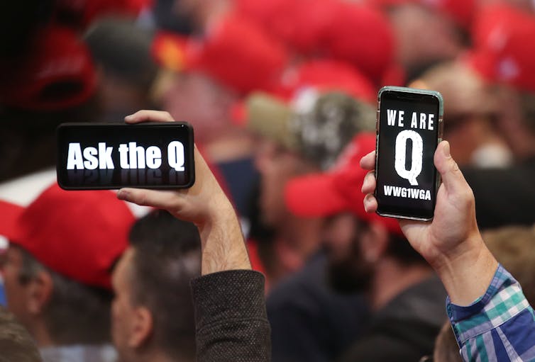Two people holding up cellphones with messages 'Ask the Q' and 'We are the Q.'
