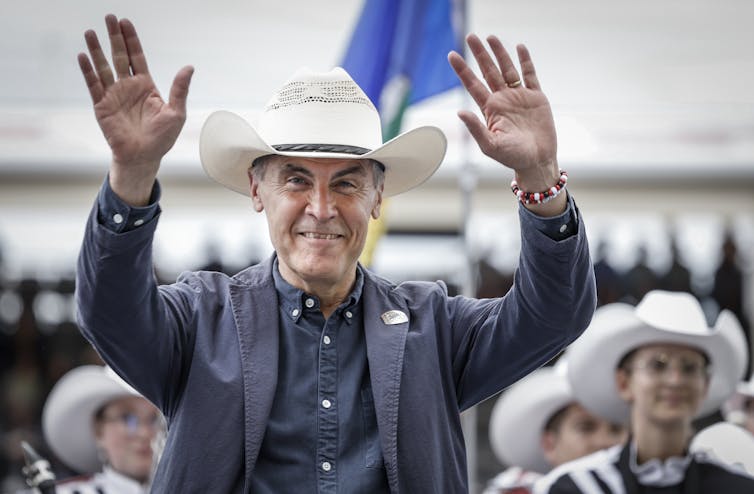 A man in a cowboy hat smiles with both arms raised.