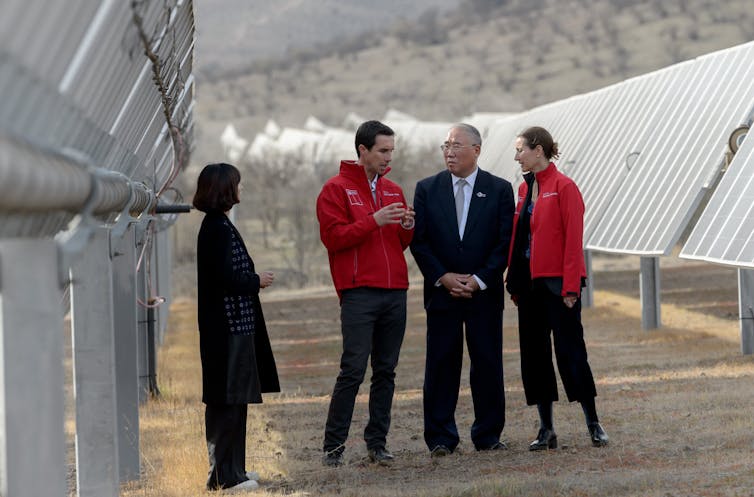 Three people talk under the shade of solar panels.