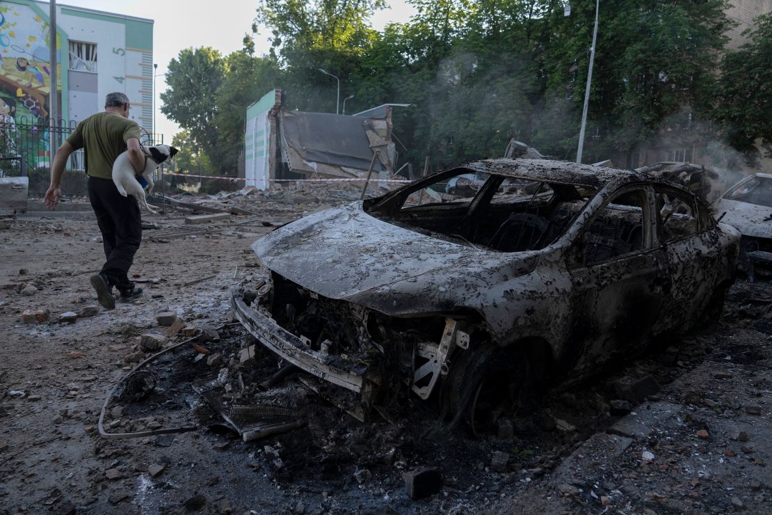 A man carrying a dog walks past the wreckage of cars following Russian drones and missile strikes on Kyiv on July 4.