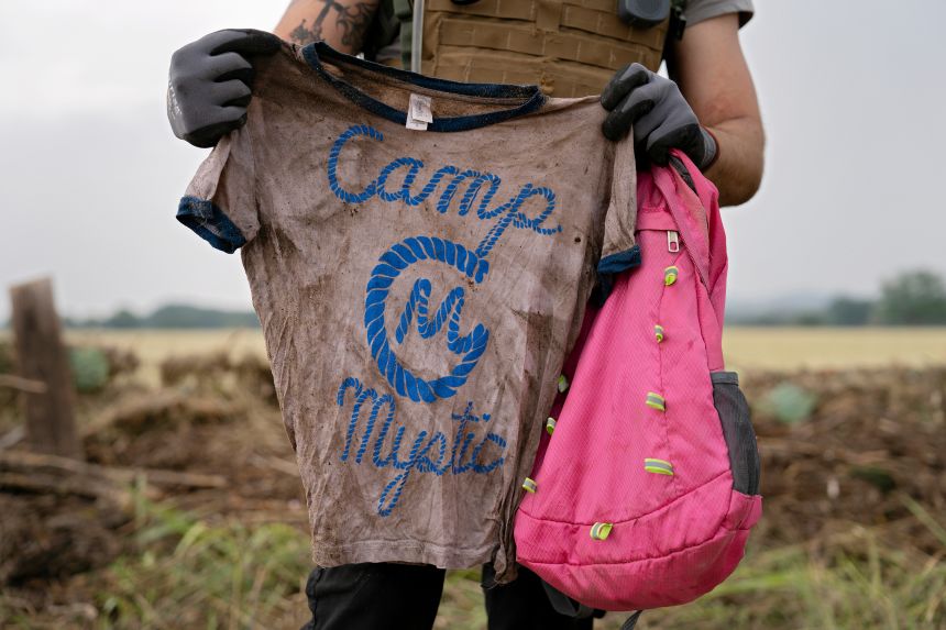 A search and rescue volunteer holds a T-shirt and backpack with the words Camp Mystic on them in Comfort, Texas, on July 6.