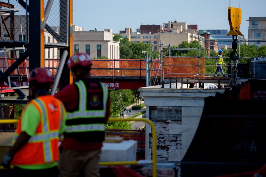 Workers walk along the roof of the Marriner S. Eccles Federal Reserve Board Building on July 24 in Washington, DC.