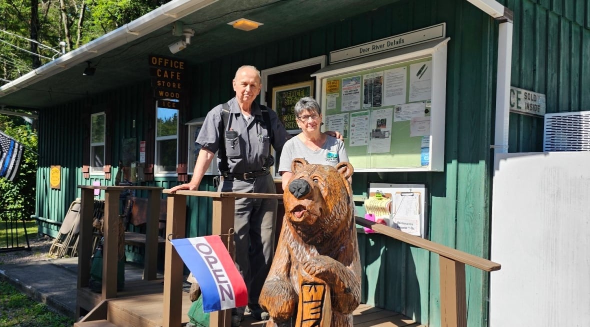 A man and a woman stand outside a green cabin