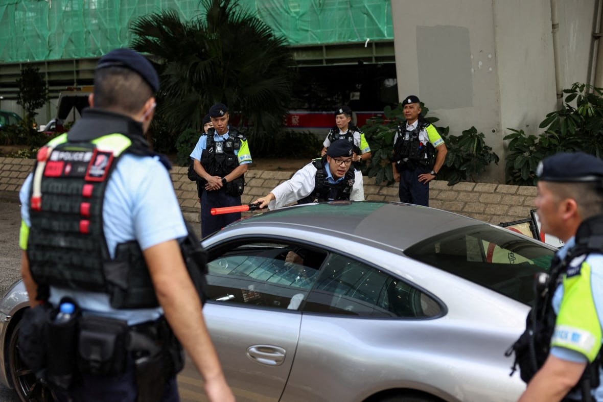 About a half-dozen police officers of Asian descent in uniform are shown surrounding a vehicle.