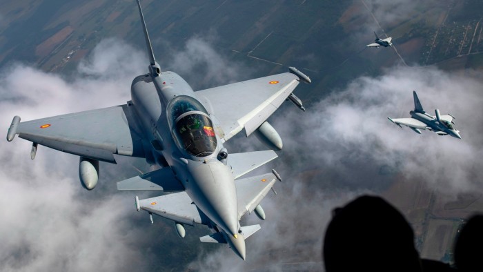 Spanish Air Force Eurofighter Typhoon jets fly on the left, and Italian Air Force Eurofighter Typhoon jets fly on the right, above clouds
