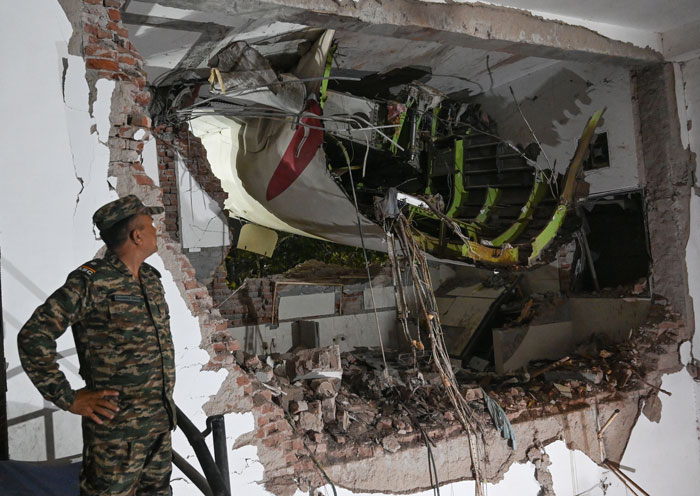 Air India pilot’s plane crash site with security guard inspecting damaged building wreckage at night.