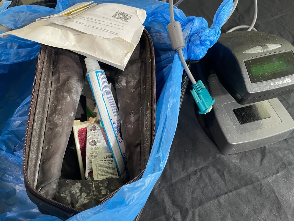 A grubby looking toiletry bag opened to show some medication and a tube of toothpaste. Next to it is a ticket scanning machine.