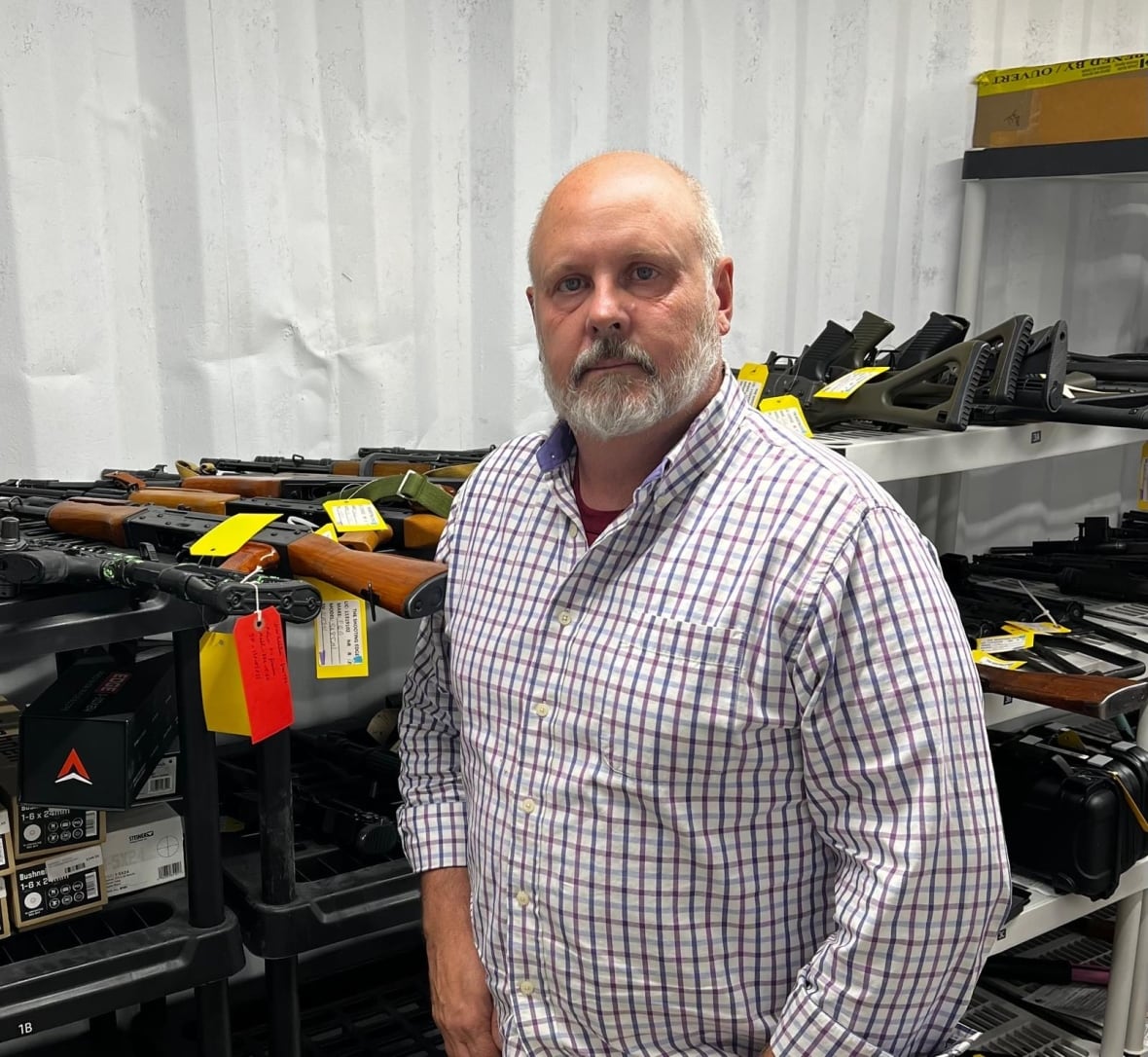 A man stands in front of a row of guns.