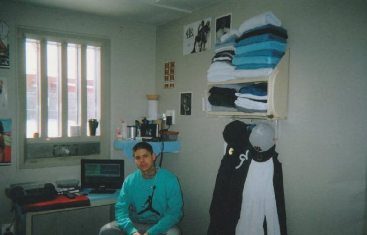 A man sits in room with a window, a computer and a shelf with towels.