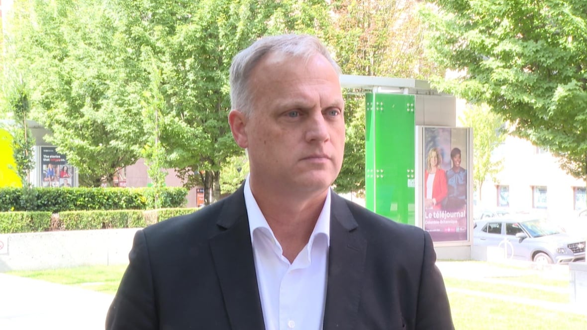 A man wearing a suit speaks in an outdoor environment.