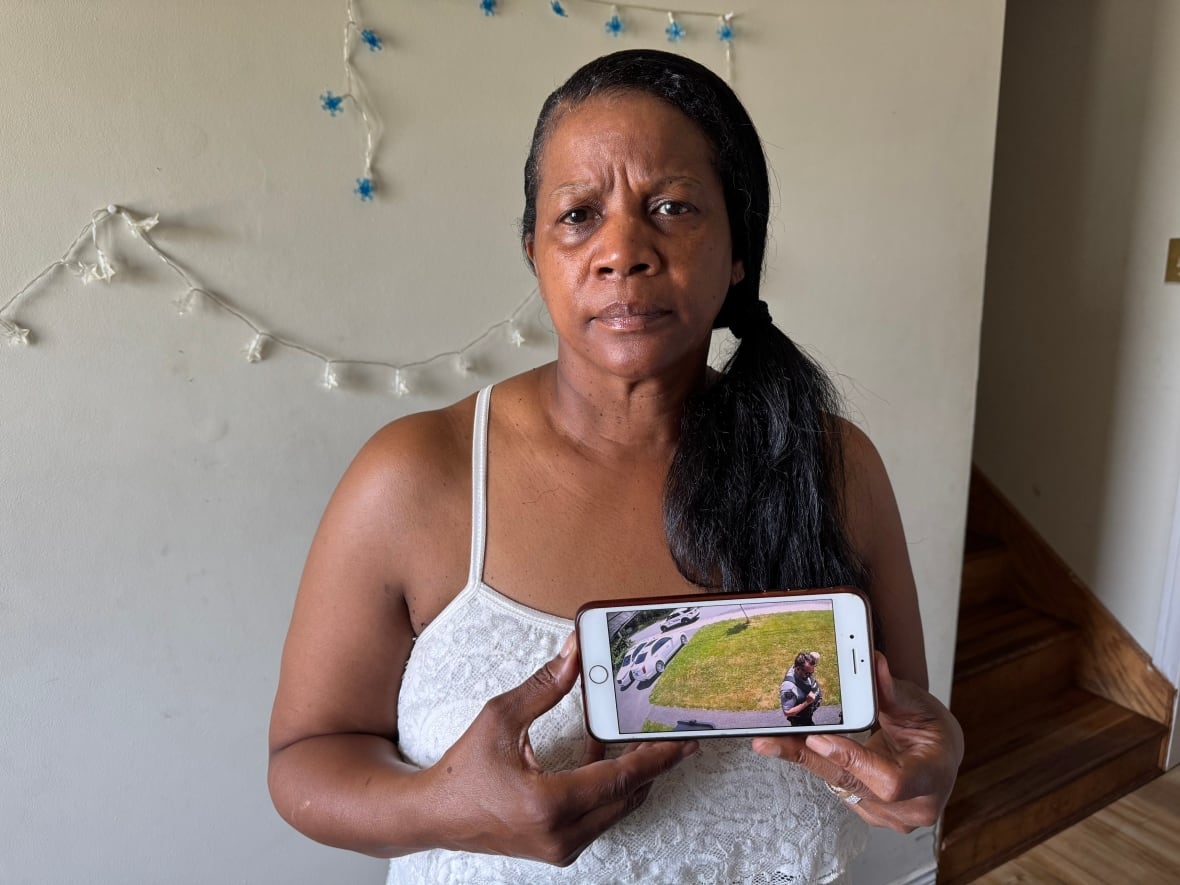 Woman with long dark brown hair in a pony tail wars a white tank top. She holds a phone.