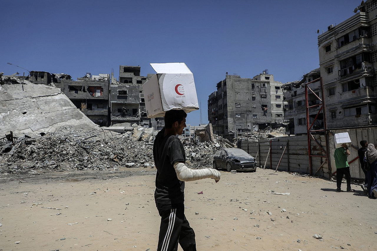 An injured Palestinian man collects humanitarian aid delivered by international organizations in Gaza City, northern Gaza Strip, June 26, 2025. (Yousef Zaanoun/Activestills)