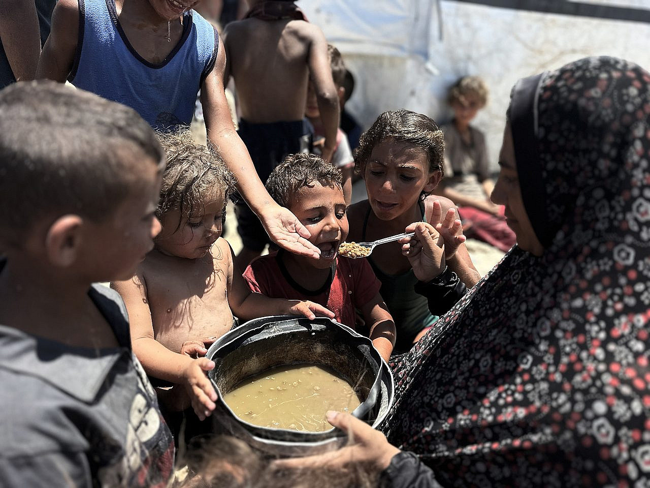 A displaced Palestinian woman feeds chldren in Al-Mawasi, southern Gaza Strip, July 13, 2025. (Doaa Albaz/Activestills)