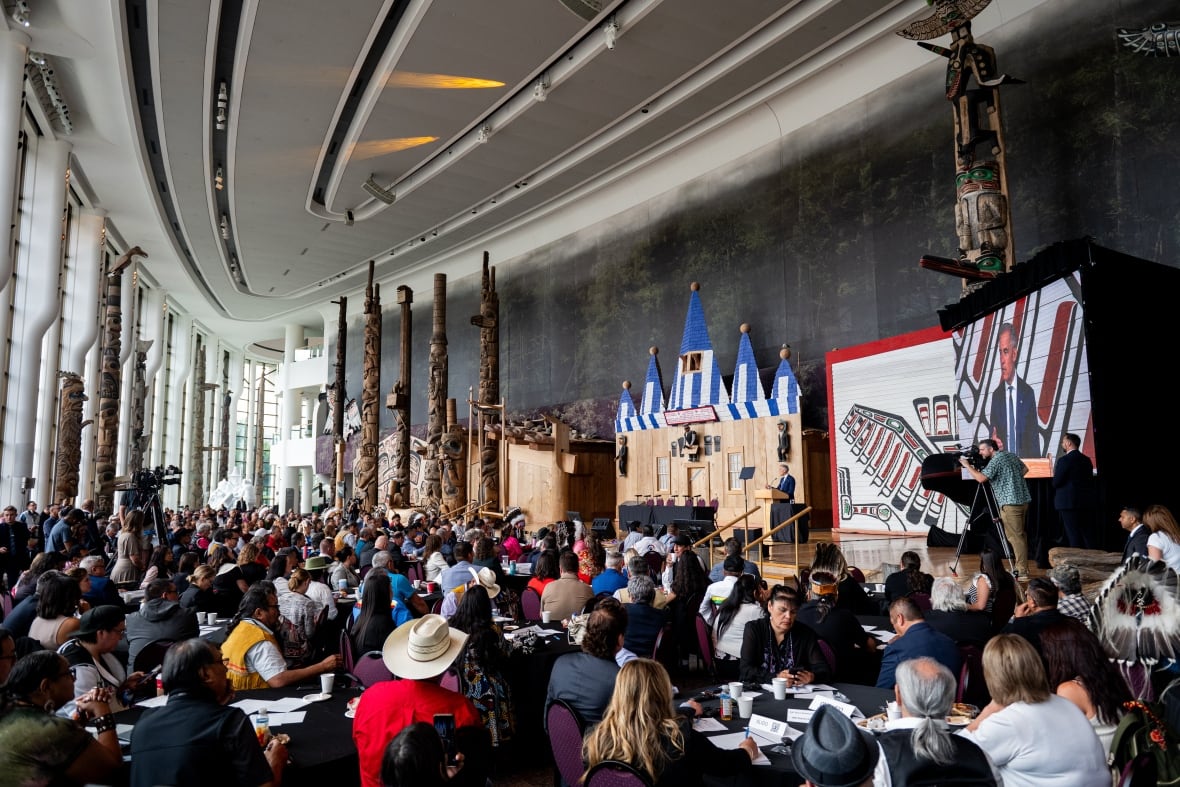 A wide shot of Indigenous leaders listening while Prime Minister Carney speaks at a podium.