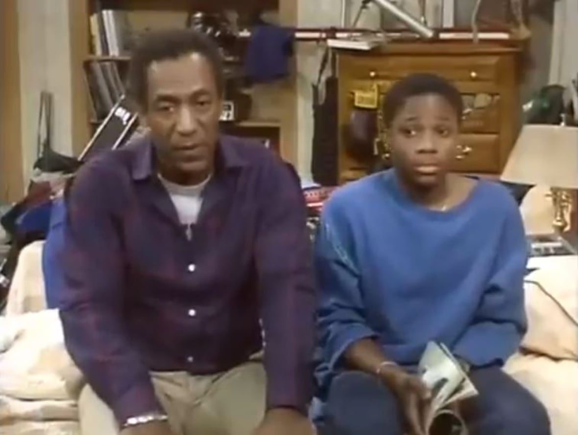 A man sits on a bed next to a teenage boy. 