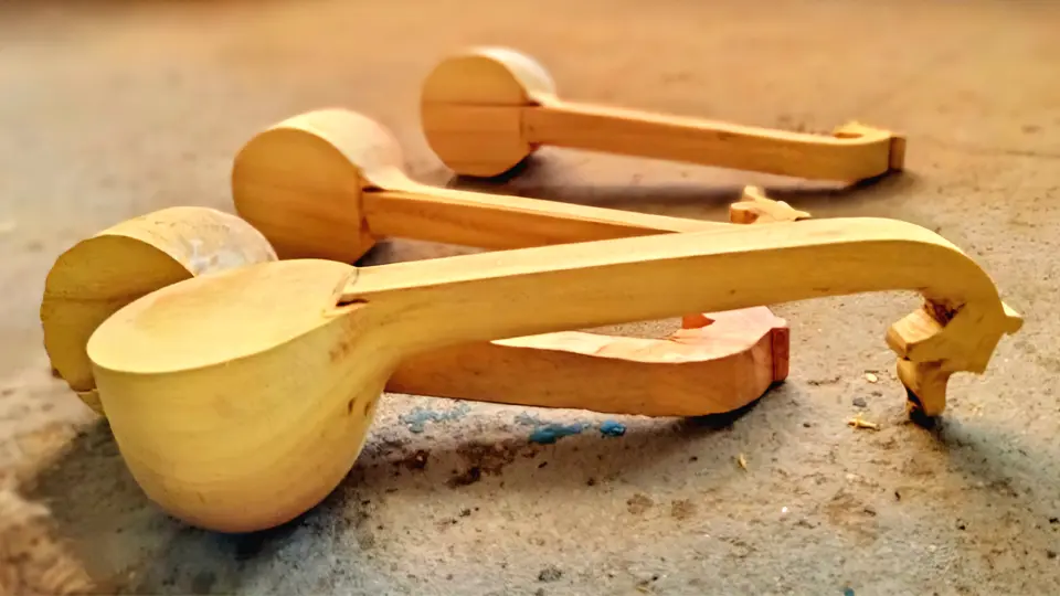Unfinished miniature Bobbili veenas made of light wood, lying on the floor in early stages of carving.