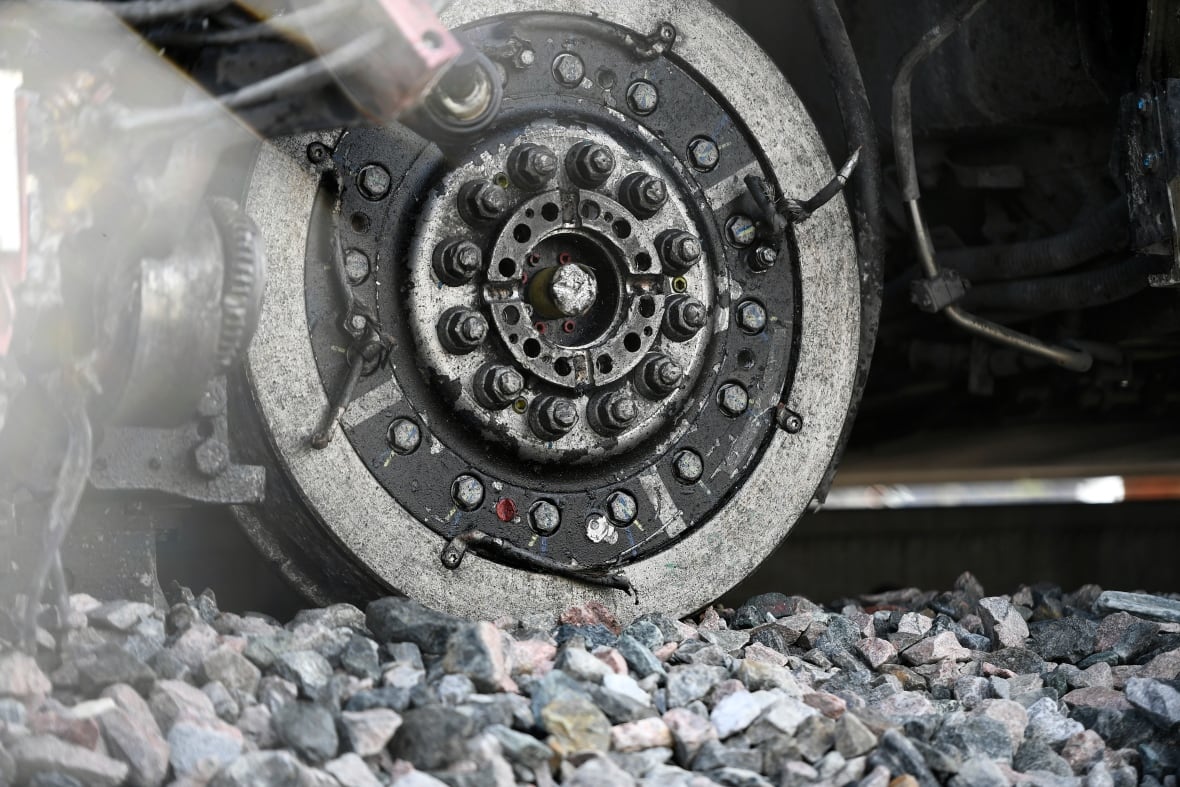 An exposed train wheel segment showing bolts rests on stone ballast
