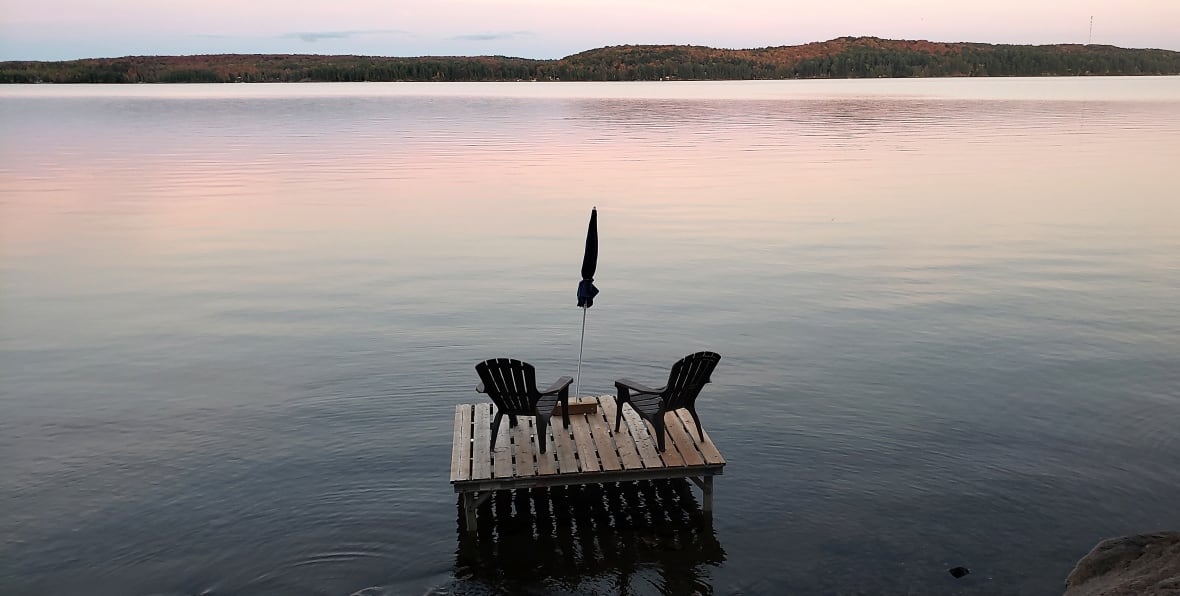 Muskoka chairs sit on a dock looking over a lake