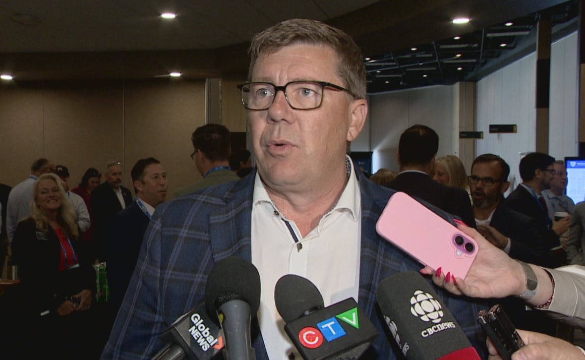 Scott Moe, dressed in a blue suit, speaks before several microphones. 