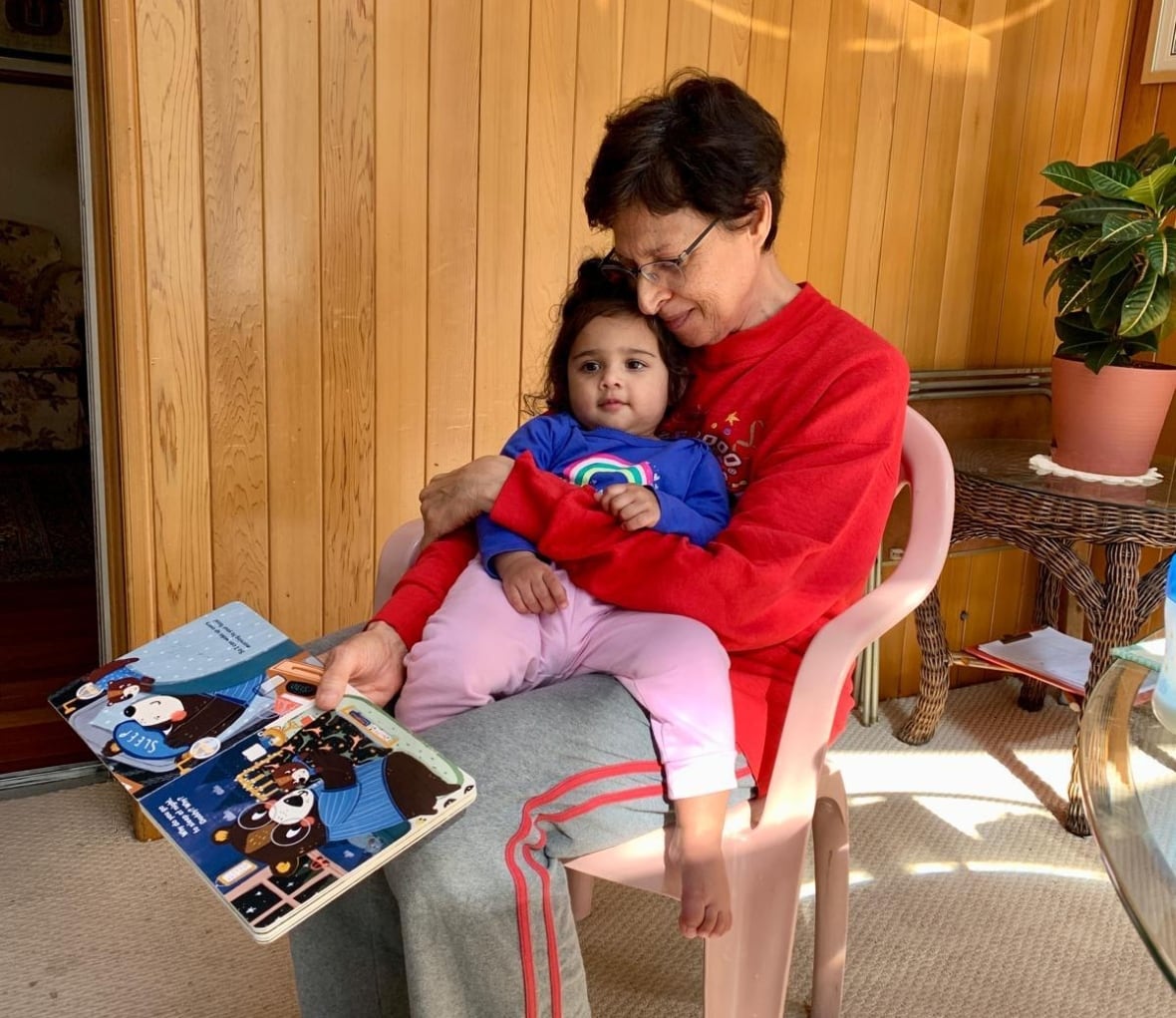 Woman sits on chair with child in lap and book in hand, smiling