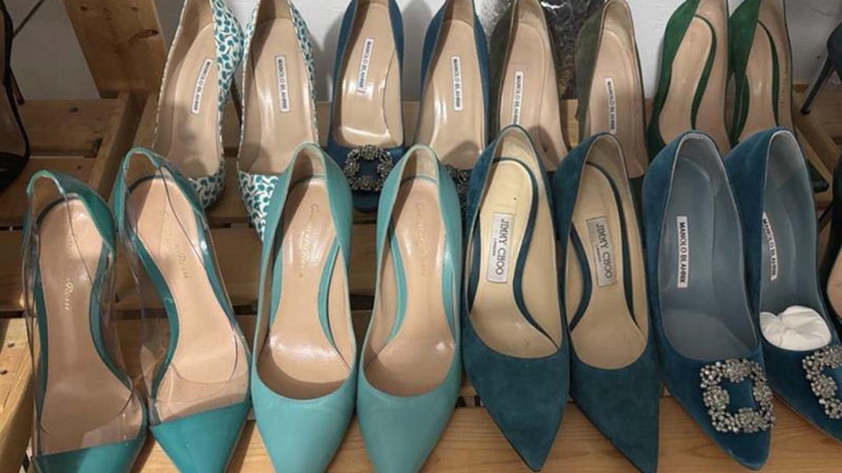 Two rows of designer shoes, including Manolo Blahniks and Jimmy Choos, sit arranged on a wooden shoe rack.