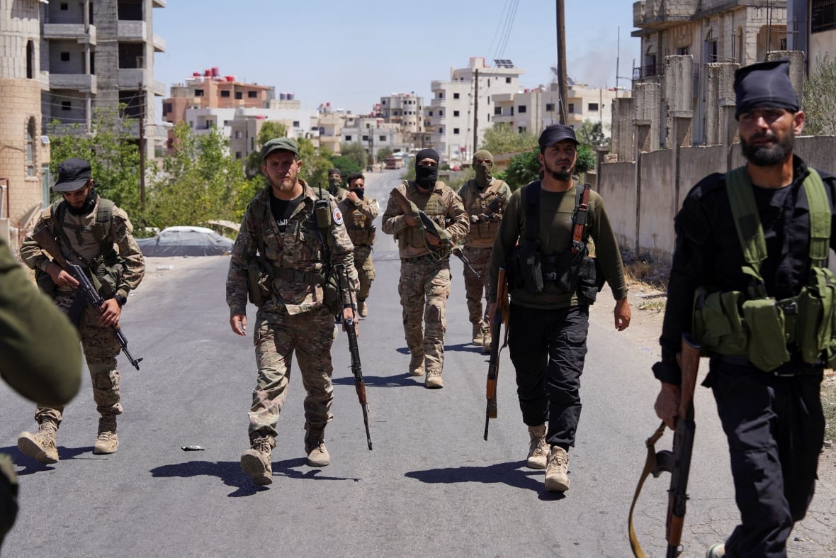Syrian security forces walk together along a street.