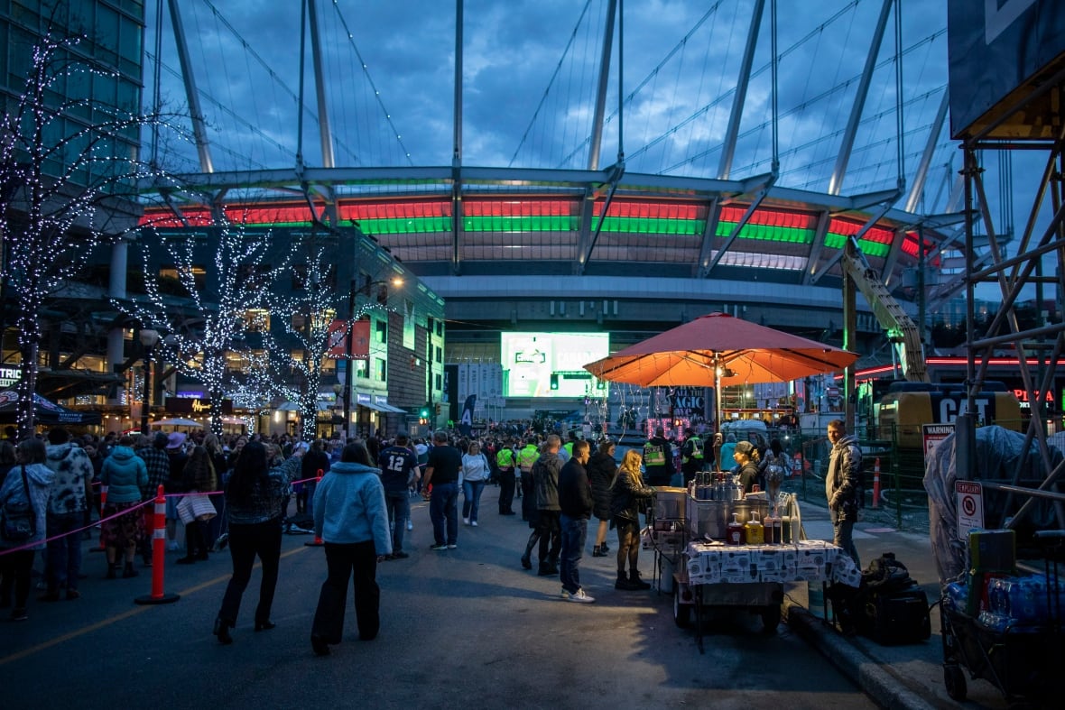 Groups of people mill around booths outside a stadium.