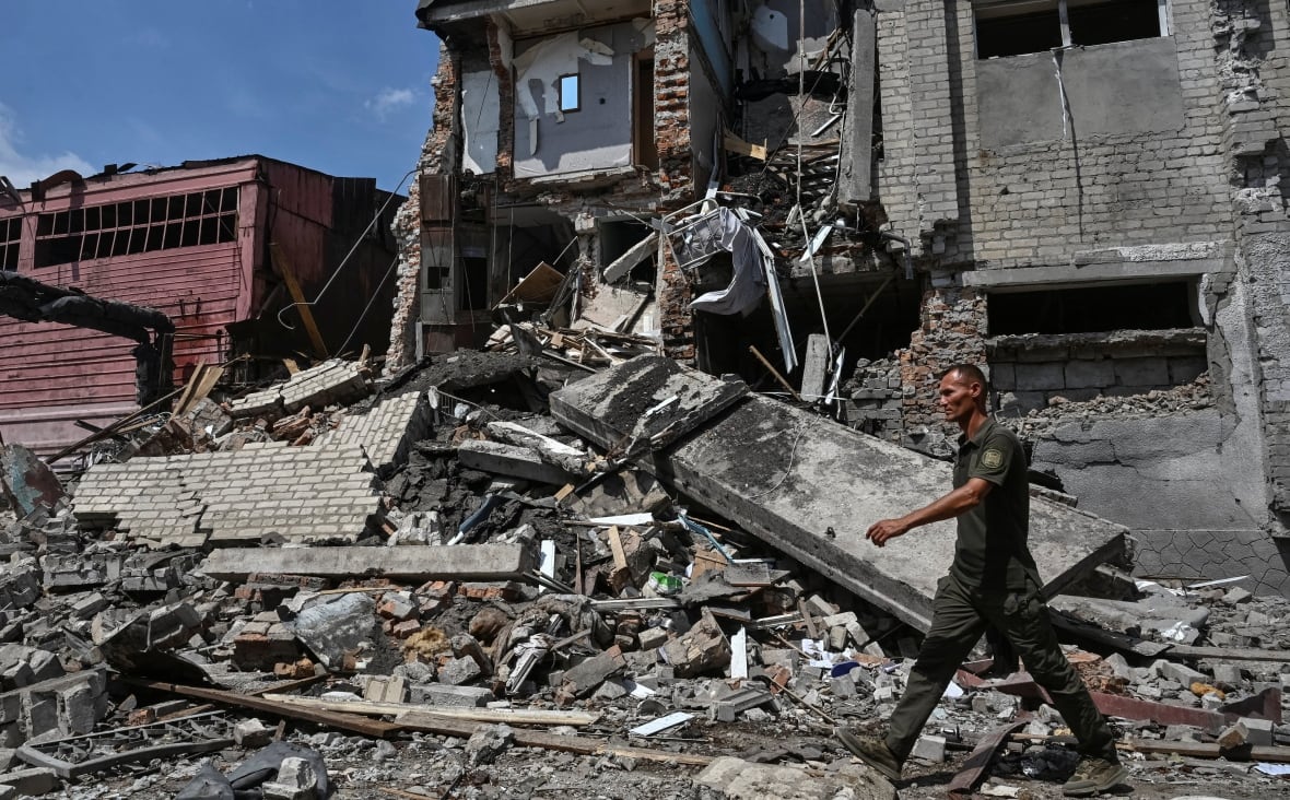 A man walks past a destroyed building. 