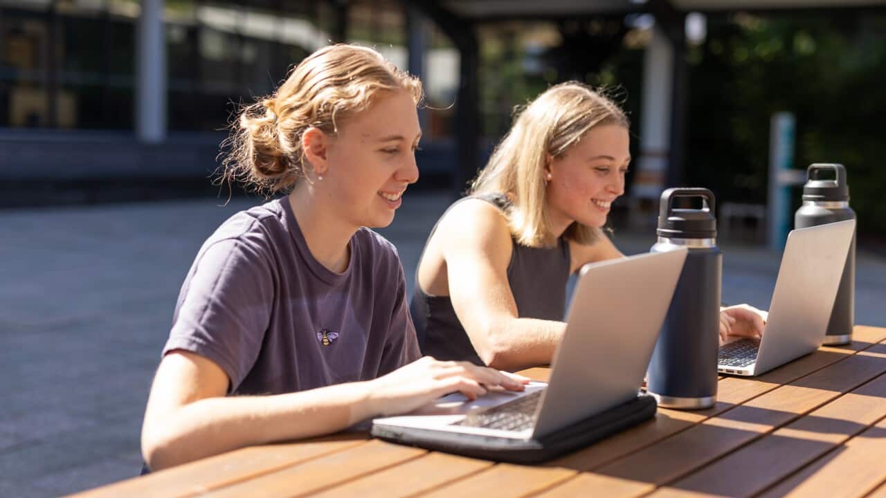 University students sitting outside at a table using their laptops.
