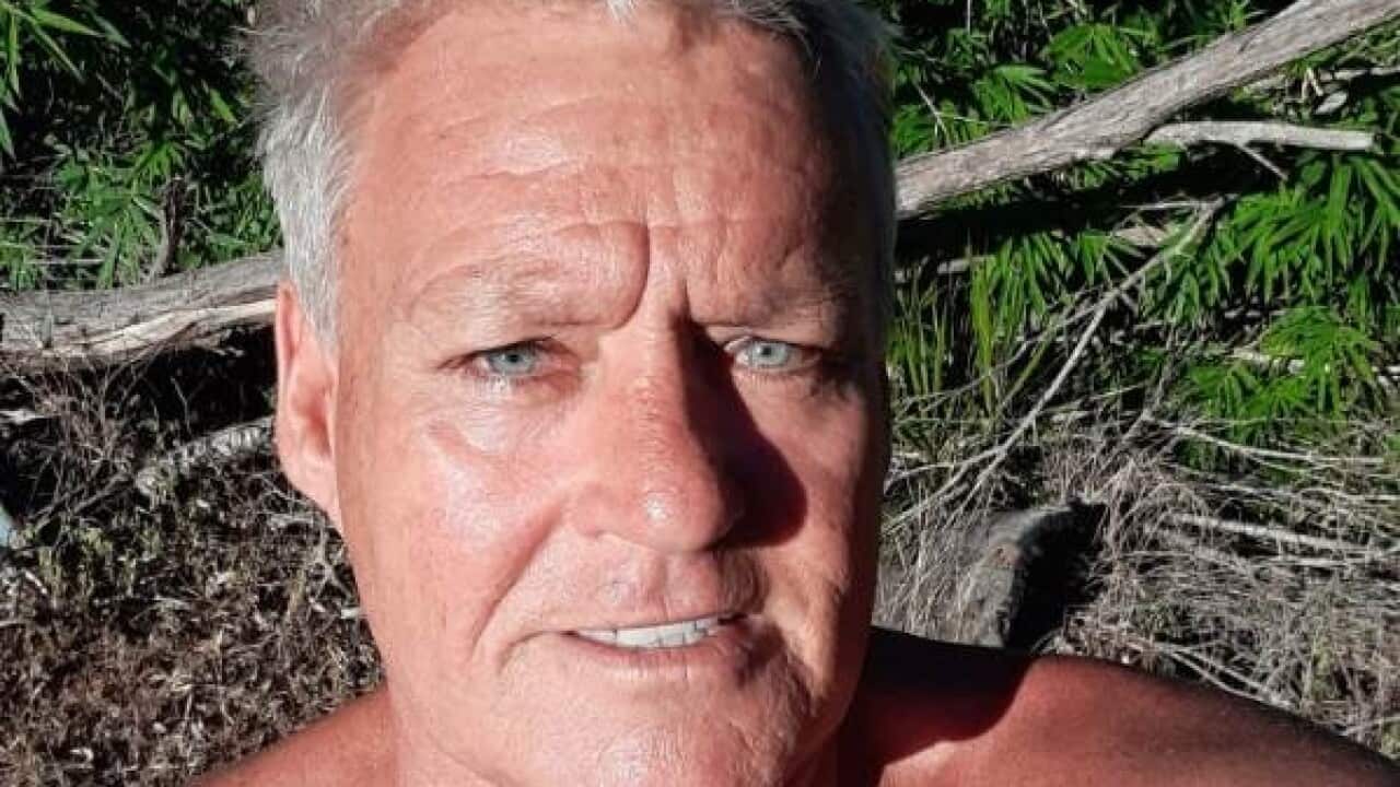 a middle aged man with white hair tanned skin takes a shirtless selfie in front of shrubbery