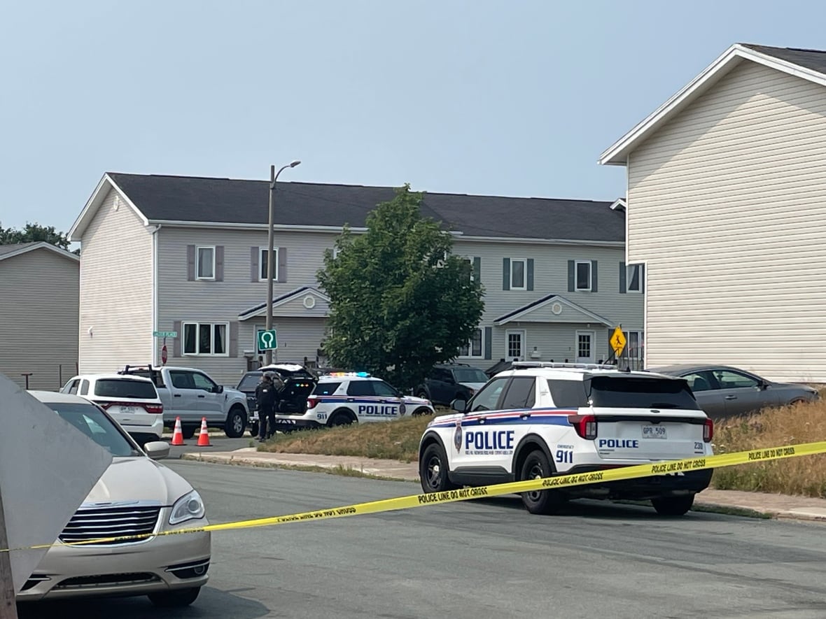 Police tape blocks street with police vehicles.