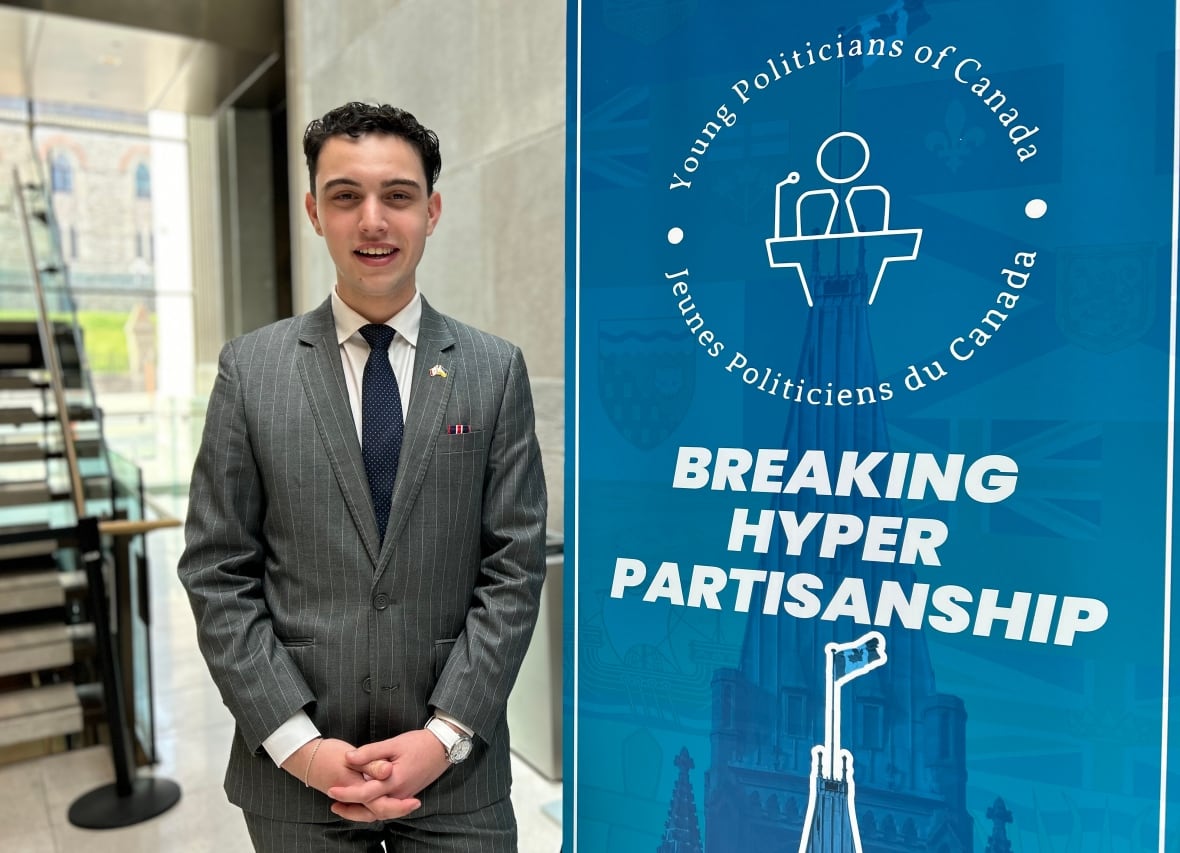 A teen in a grey suit poses for a photo in front of a banner.
