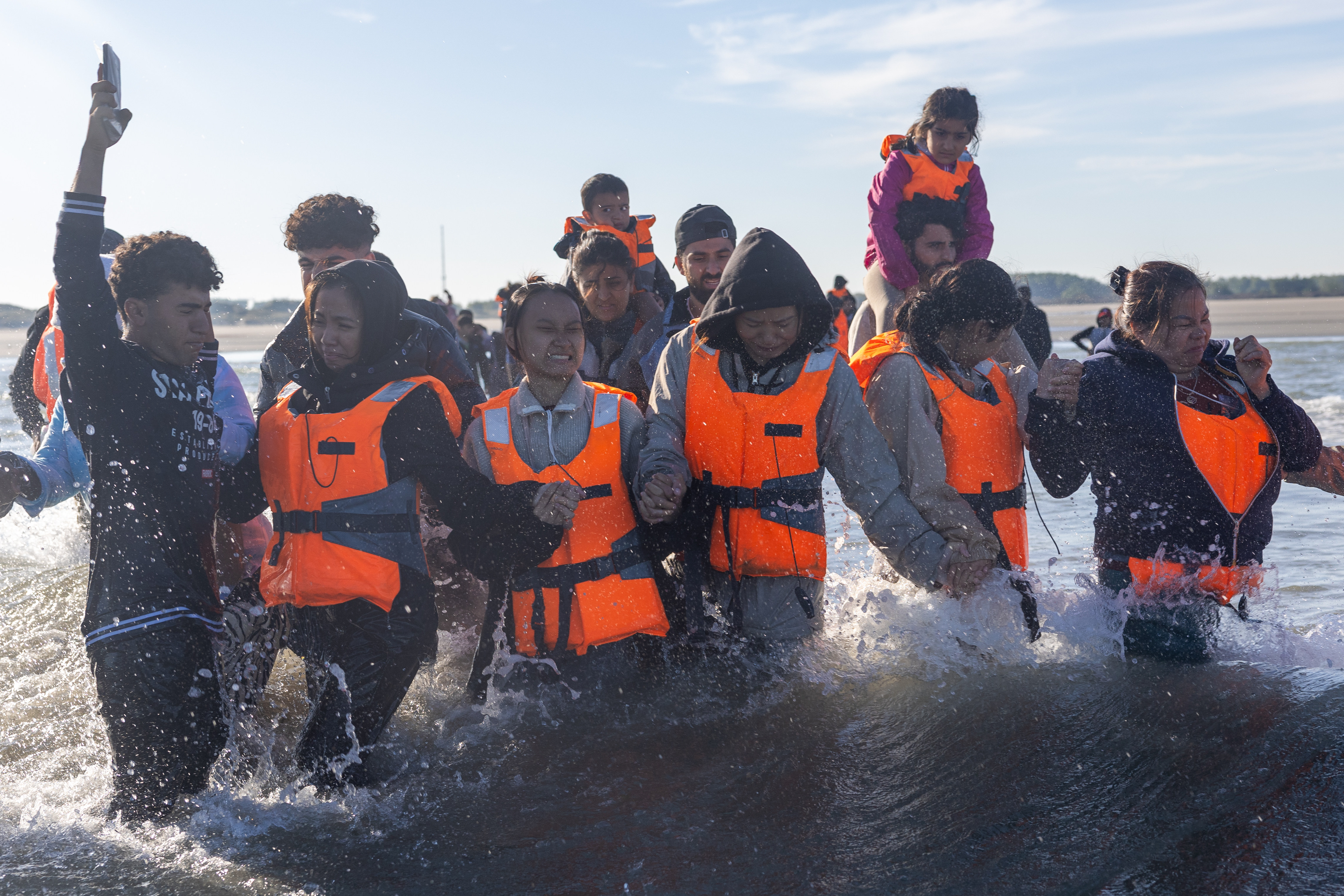 Migrants in life vests wade into the water to board a small boat.