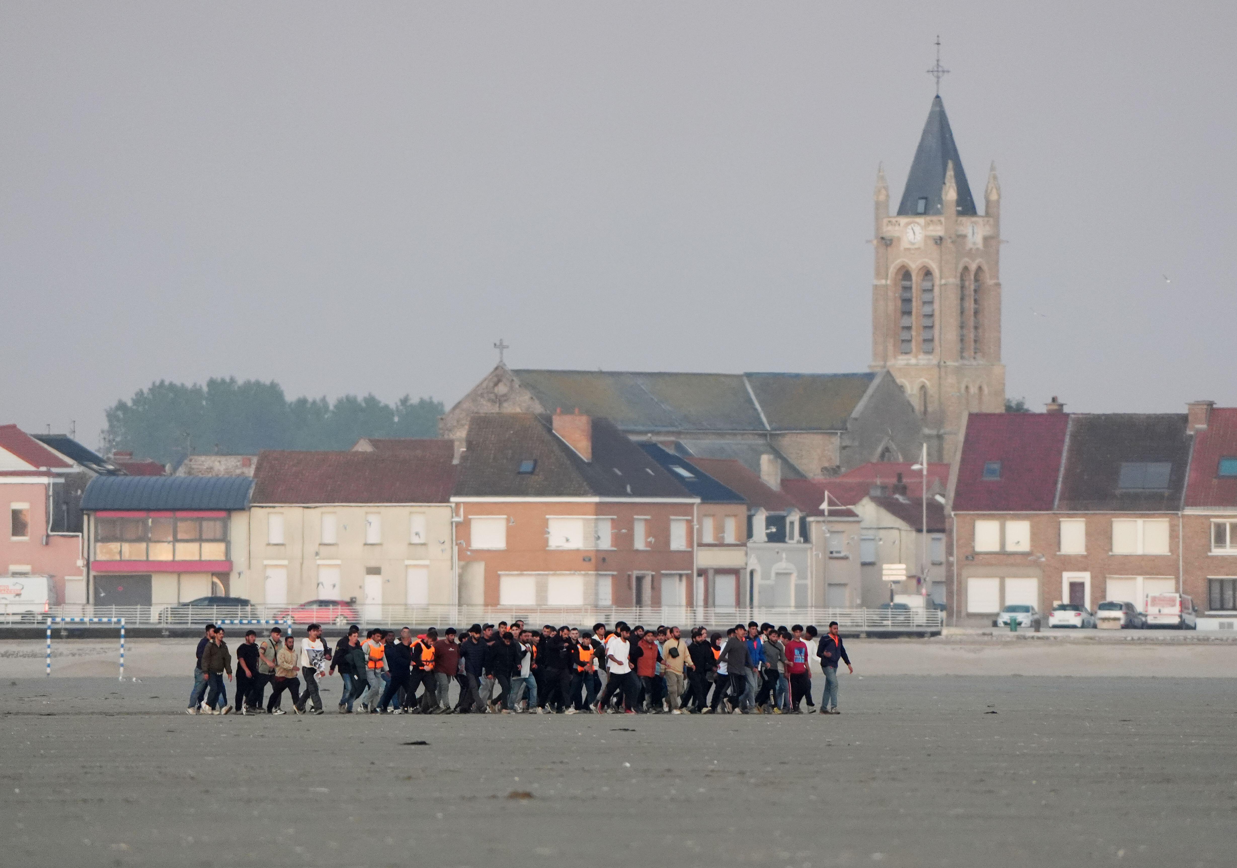 Migrants running across a beach in Gravelines, France, toward a small boat.