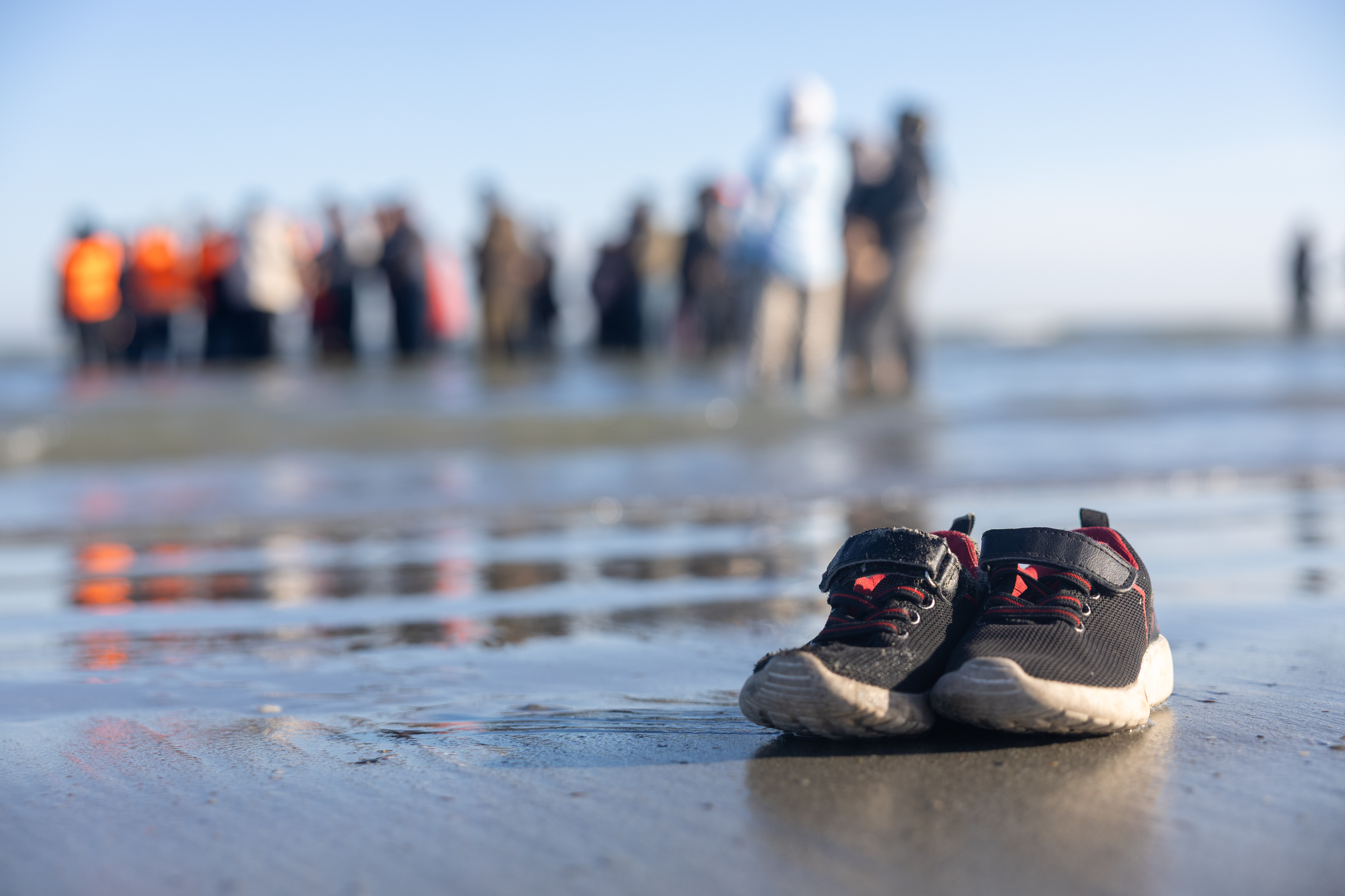 Child's shoes left on a beach as migrants board a boat.