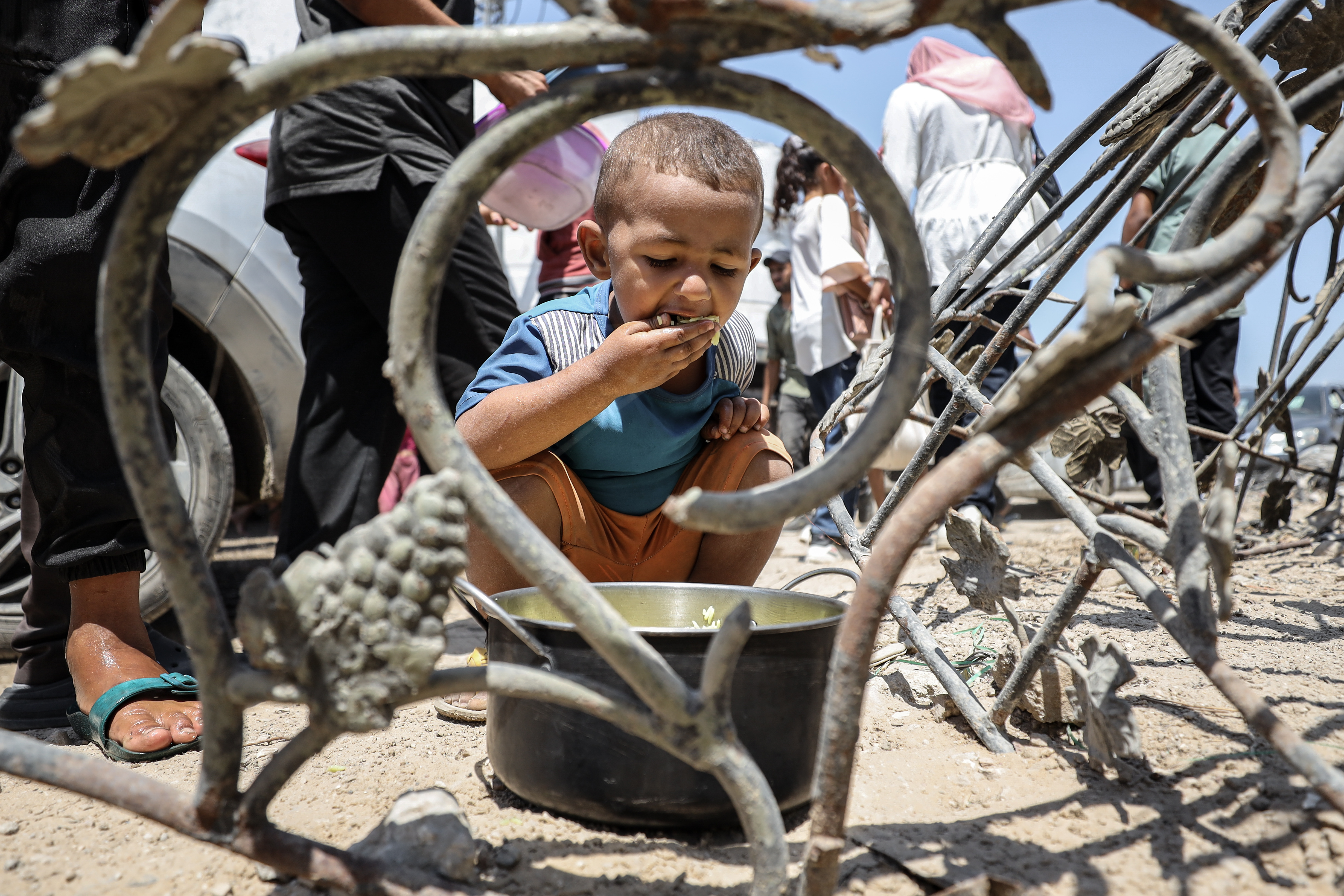 A young Palestinian child eats from a pot of food amidst a crowd waiting for food distribution in Gaza.