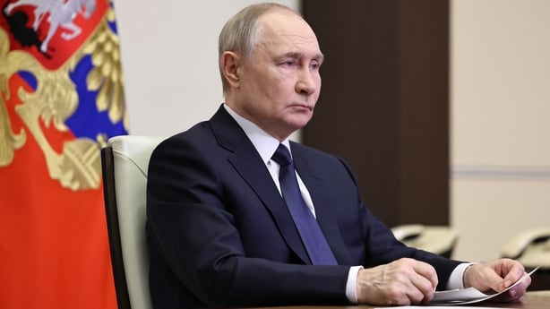 Russian President Vladimir Putin sits at a desk in front of a Russian flag.