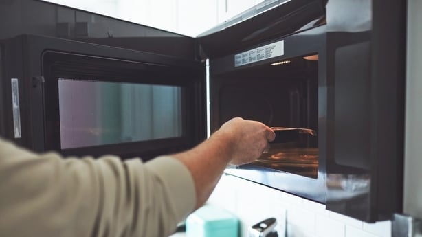 a man opening a microwave and putting in a ready meal