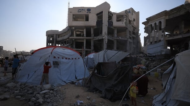 Refugees are seen in tents in front of damaged buildings in Gaza