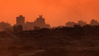 A desolate ground surface seen in Gaza with damaged buildings in the background with an orange hue as the sun sets