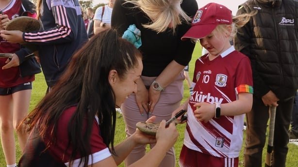 A girl wearing a maroon Galway jersey meets a player who is signed her hurley with a marker