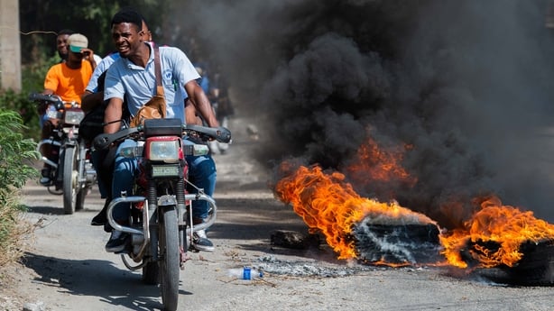 People drive motorcycles past burning tyres during a demonstration at Bourdon near the Villa D'Accueil in Port-au-Prince, Haiti