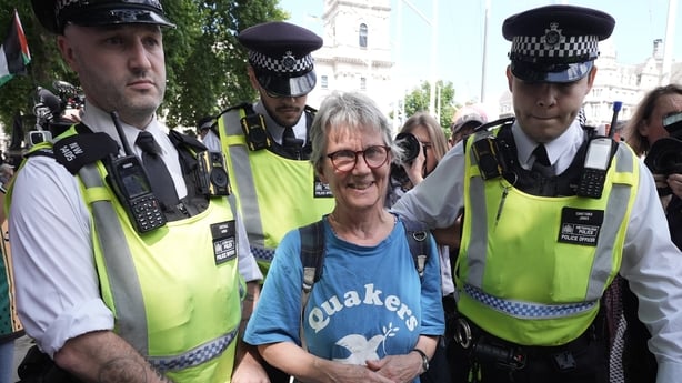 A woman wearing a blue t shirt smiles as two police officers lead her away from a protest