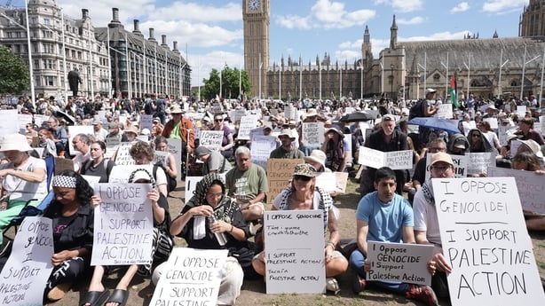 Hundreds of people holding white placards with writing on them sit in parliament square in London