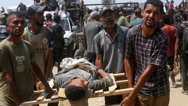Four men carry a fifth man on a makeshift wooden stretcher in Gaza