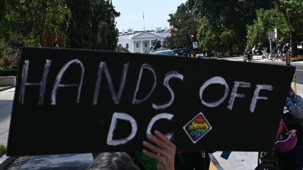 A person holds up a black sign that read 'hands off DC' with the white house in the back ground
